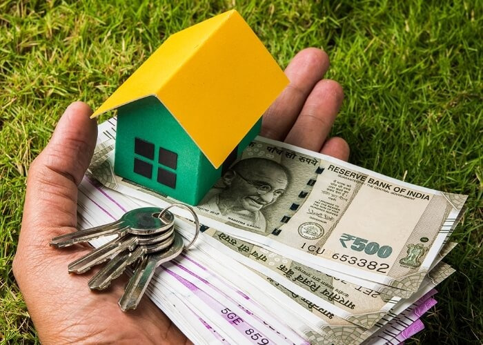 Hand holding house keys, Indian currency notes and a miniature house symbolizing home buying and housing finance